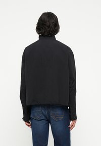 Črna skrajšana jakna iz lahkega materiala, s visokim ovratnikom, dolgimi rokavi in preprosto silhueto. V paru z denim hlačami.