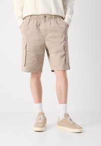 Calções cargo bege com cintura elástica, dois bolsos laterais e dois grandes bolsos nas pernas. Combinados com sapatilhas de cor clara e meias brancas.