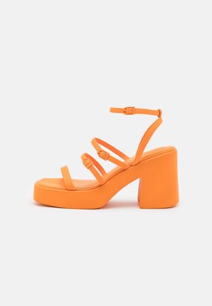 Orange chunky platform-hæl sandal med fire justerbare spænderemmer og en ankelrem, vist mod en hvid baggrund.