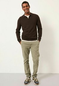 Brauner Pullover mit langen Ärmeln und Reißverschlusskragen, kombiniert mit hellgrünen Chinos und braunen, grauen und weißen Sneakers. Einfaches, lässiges Design.