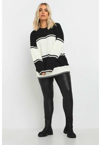 Stickad tröja med svart och vit randig design, vida ärmar och ribbad struktur. Kombinerad med svarta läderleggings och stövlar.