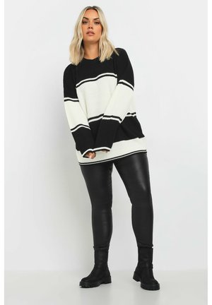Gebreide trui met een zwart-wit gestreept ontwerp, brede mouwen en een geribbelde textuur. Gecombineerd met zwarte leren legging en laarzen.