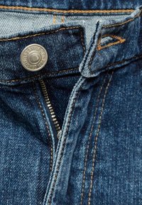 Gros plan sur un jean en denim bleu déboutonné, avec un bouton en métal visible et des coutures orange autour de la ceinture et de la zone de la fermeture éclair.