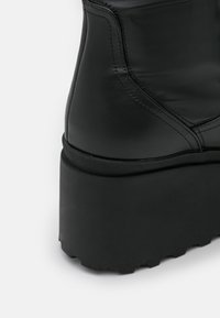 Černá kožená kotníková bota s silnou platformovou podrážkou, s hladkým povrchem a zesílenými švy podél švů.