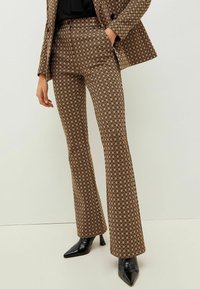 Braun gemusterte, schicke Schlaghosen mit geometrischem Design, hoher Taille, Seitentaschen und glatter Textur. Kombiniert mit schwarzen hohen Schuhen.