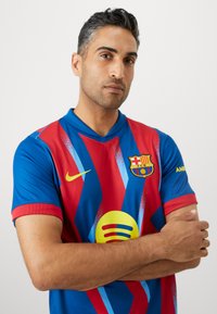 Barcelonos FC marškiniai su raudonai mėlynomis dryžuotomis, grafiniu raštu, Nike logotipu ir Spotify logotipu. Trumpomis rankovėmis ir V formos iškirpte.