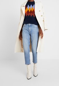 Svetr z pleteniny s diamantovým vzorem v námořnické modré, oranžové, žluté a modré barvě, kombinovaný se světle modrými džínami s rovnými nohavicemi a krémovými kotníkovými botami.