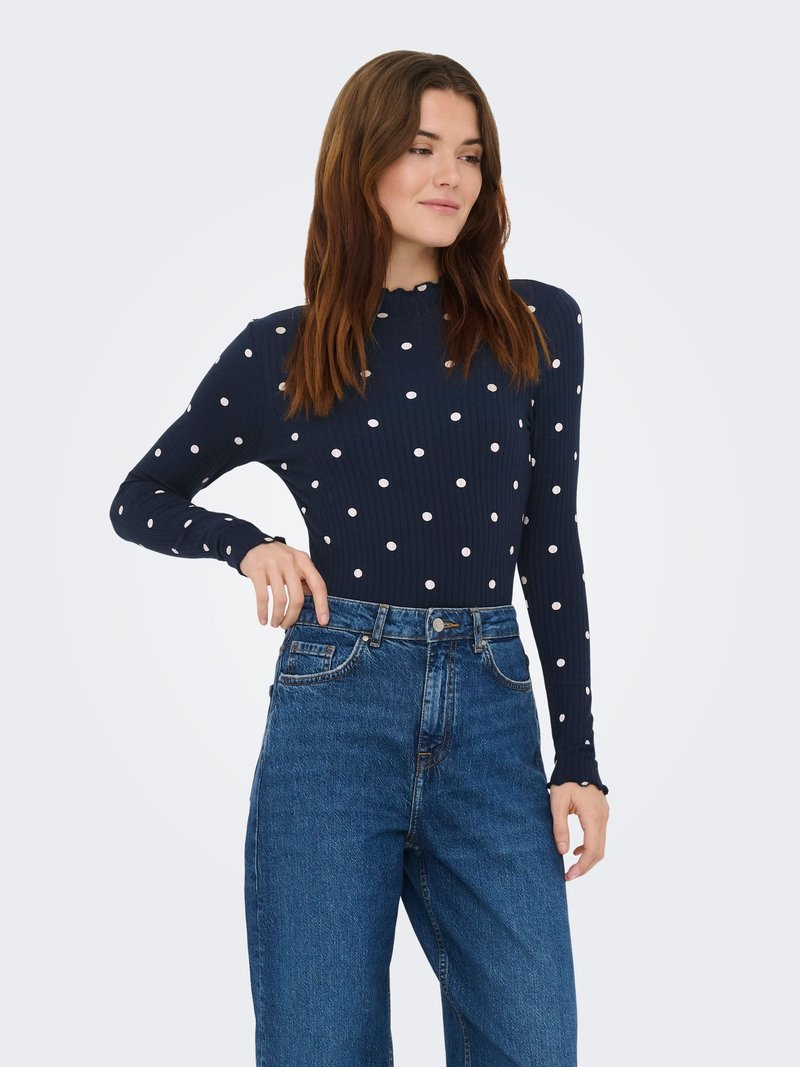 Marineblå langærmet top med hvide polkaprikker, ribdet tekstur og bølget halsudskæring, kombineret med højttaljede blå denimjeans.