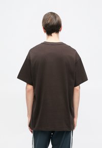 Ruda medvilninė marškinėlių su laisvu kirpimu, trumpomis rankovėmis ir apvaliu iškirpimu. Sklandus audinys, minimalus dekoravimas, derinami su tamsiomis sportinėmis kelnėmis.