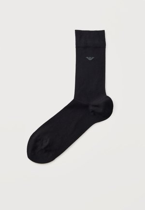 Chaussette noire mi-mollet avec un bord-côte et un petit logo d’aigle gris, présentée sur un fond clair.