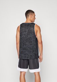 Zwarte mesh sporttanktop met een gestructureerd grafisch patroon, geaccentueerd met oranje en blauwe bies. Draag het over zwarte shorts met witte strepen.