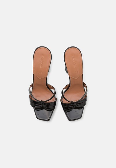 Schwarze Lackleder-Mules mit offener Zehenpartie und quadratischer Zehenform, ausgestattet mit dünnen Knögelriemen und glatten, tanfarbenen Innensohlen, die mit dem Markennamen geprägt sind.