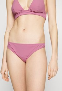 Biquíni de dois peças numa suave cor rosa, apresentando um top triangular e um fundo de biquíni combinando; textura suave, design minimalista.