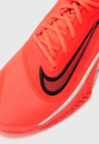 Klarröd Nike-sko med en texturerad ovandel, med svarta logotypdetaljer, platta snören och en mönstrad gummisula för bra grepp.