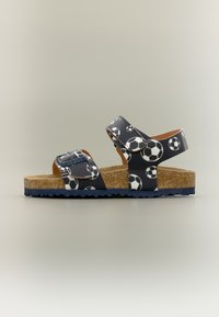 Παιδικό σανδάλι με σόλα φελλού και μαύρα λουριά με εκτύπωση λευκών και μαύρων ποδοσφαιρικών μπαλών, δύο ρυθμιζόμενα κλεισίματα με αγκράφα και βέλκρο.