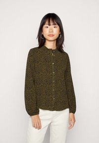 Blusa de manga longa, verde-oliva, com padrão de manchas pretas, apresentando um colarinho franzido e fecho de botões à frente, e punhos de mangas franzidos.