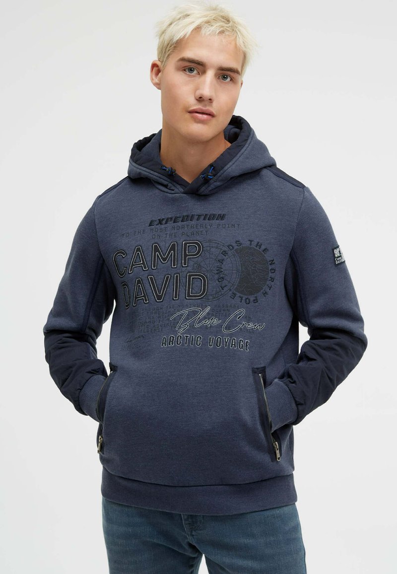 Navy blue hoodie with a front graphic print, featuring "Camp David" text. It has contrasting dark blue sleeves and zipped side pockets.