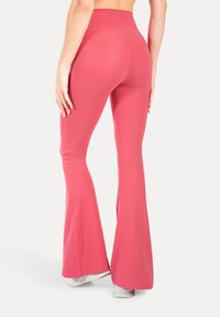 Leggings a campana aderenti di un brillante rosa, con una texture liscia e un alto punto vita. Presentano dettagli di cucitura lungo la cucitura.