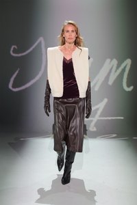 Bela jagnjeća kratka jakna preko temnega žametnega topa, rjave naborkane hlače in dolgi črni usnjeni rokavici, v kombinaciji z črnimi čevlji do kolen.