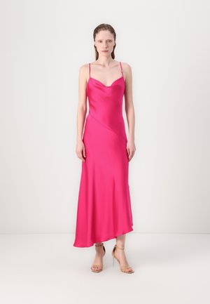 Robe à slip en satin rose avec des bretelles fines, décolleté plongeant et ourlet asymétrique. Portée avec des sandales à talons hauts nude.