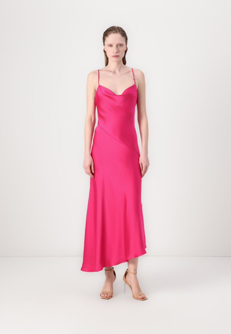 Pink satin slip dress with thin straps, plunging neckline, and asymmetrical hemline. Worn with nude high-heeled sandals.