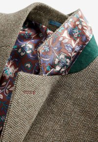 Herringbone-patterned brown blazer with a floral, purple-patterned silk lining and green accent on the collar. Textured wool fabric.