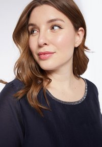 Top blu navy con scollatura rotonda e dettagli in perline argentate. Il tessuto sembra morbido, con una trama liscia e una vestibilità ampia.