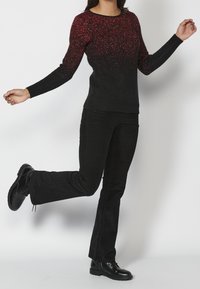 Schwarzer und roter Gradient-Pullover mit langen Ärmeln, Rundhalsausschnitt und strukturiertem Finish, kombiniert mit schwarzen weit geschnittenen Hosen und schwarzen Schnürstiefeln.