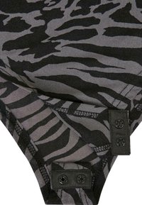 Tkanina s crno-sivim uzorkom zebra sa glatkom teksturom, koja ima dva kopčanja na dugmadi i kontrastnu šavovima duž rubova.