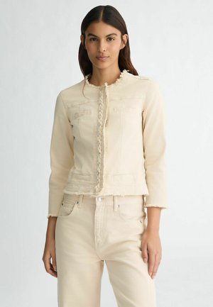 Giacca di denim beige con bordi sfrangiati, maniche lunghe e due tasche sul petto. Presenta una chiusura anteriore intrecciata e un design aderente.