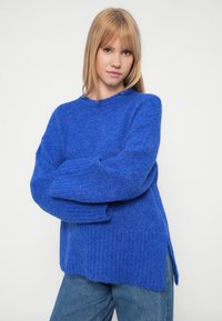 Σαλοπέτα πλεκτή σε κοβαλτίνο μπλε χρώμα με ριμπ τελείωμα και φαρδιά μανίκια, διαθέτοντας στρογγυλή λαιμόκοψη και πλαϊνές σχισμές για ευκολία κινήσεων.