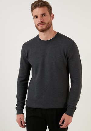 Mørkegrå textured sweater med rund hals og lange ærmer, der har et diskret mønster og kontrasterende hvid kant omkring halsudskæringen.