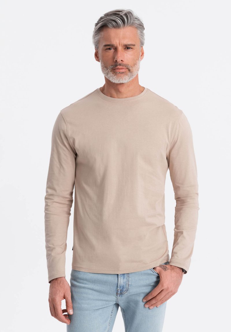 Beige långärmad t-shirt i mjukt tyg, med rund halsringning och åtsittande ärmar, i kombination med ljusblå jeans.