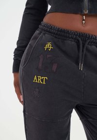 Svarta träningsbyxor i bomullsblandning med resårmidja. Har gul broderi av symboler och texten "17" och "ART", tillsammans med en subtil design.