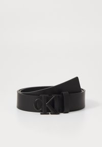 Cintura in pelle nera con una superficie liscia, dotata di una fibbia in metallo nero con il logo "CK". Il design è minimalista e elegante.