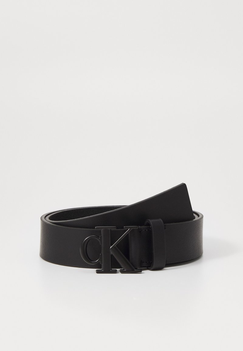 Cintura in pelle nera con una superficie liscia, dotata di una fibbia in metallo nero con il logo "CK". Il design è minimalista e elegante.