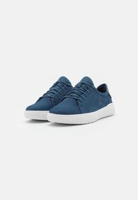 Zapatillas de ante azul marino con suelas de goma blanca, que presentan una lengüeta de malla texturizada, cordones y un pequeño logo en el costado.