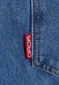 Kék farmeranyag narancssárga varrással és egy kis piros szövetcímkével, amely a zseb varrásához van rögzítve.