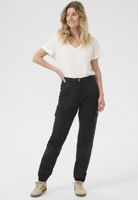 Svarta cargobyxor med elastiska säkringar, framfickor och en justerbar midja. T-shirten är krämfärgad, tillverkad av mjukt tyg med V-krage.
