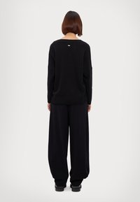 Maglione nero a maglia con schiena bassa, abbinato a pantaloni neri a gamba larga. Presenta dettagli di cucitura discreti e maniche ampie. Design semplice.