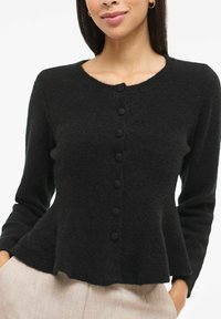 Melns kardigans no mīksta, strukturēta auduma, ar apaļu kakla izgriezumu, priekšā aizpogājams un ar uzplečiem paplašinātu apakšu.