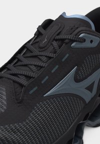 Μαύρο και γκρι αθλητικό παπούτσι με ύφασμα από δίχτυ, λεπτομερείς ραφές, κορδόνια με σχέδιο και λογότυπο στην πλευρική επιφάνεια κοντά στα κορδόνια.