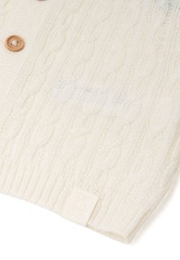 Béžový svetr z kabelkového úpletu s dřevěnými knoflíky a malou etiketou s logem zajíčka na lemu. Měkká textura a žebrované detaily na manžetách.