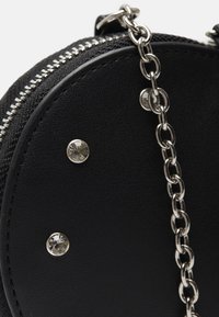 Borsa circolare nera con superficie texture, zip argentata e tracolla a catena. Presenta borchie decorative argentate e una finitura liscia.