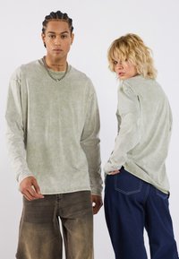 Langermet, falmet grønn skjorte i vasket bomull, kombinert med løse brune shorts og mørk blå jeans, som viser uformelle, avslappede passformer.