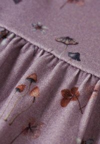 Tissu violet doux avec une couture froncée, décoré de petites illustrations de champignons, de feuilles et de fleurs dans des tons terreux atténués.