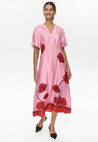 Pink satin midi dress with short flutter sleeves, a V-neck, floral red poppy print, and a gathered waist. Features a red hem with black stripes.