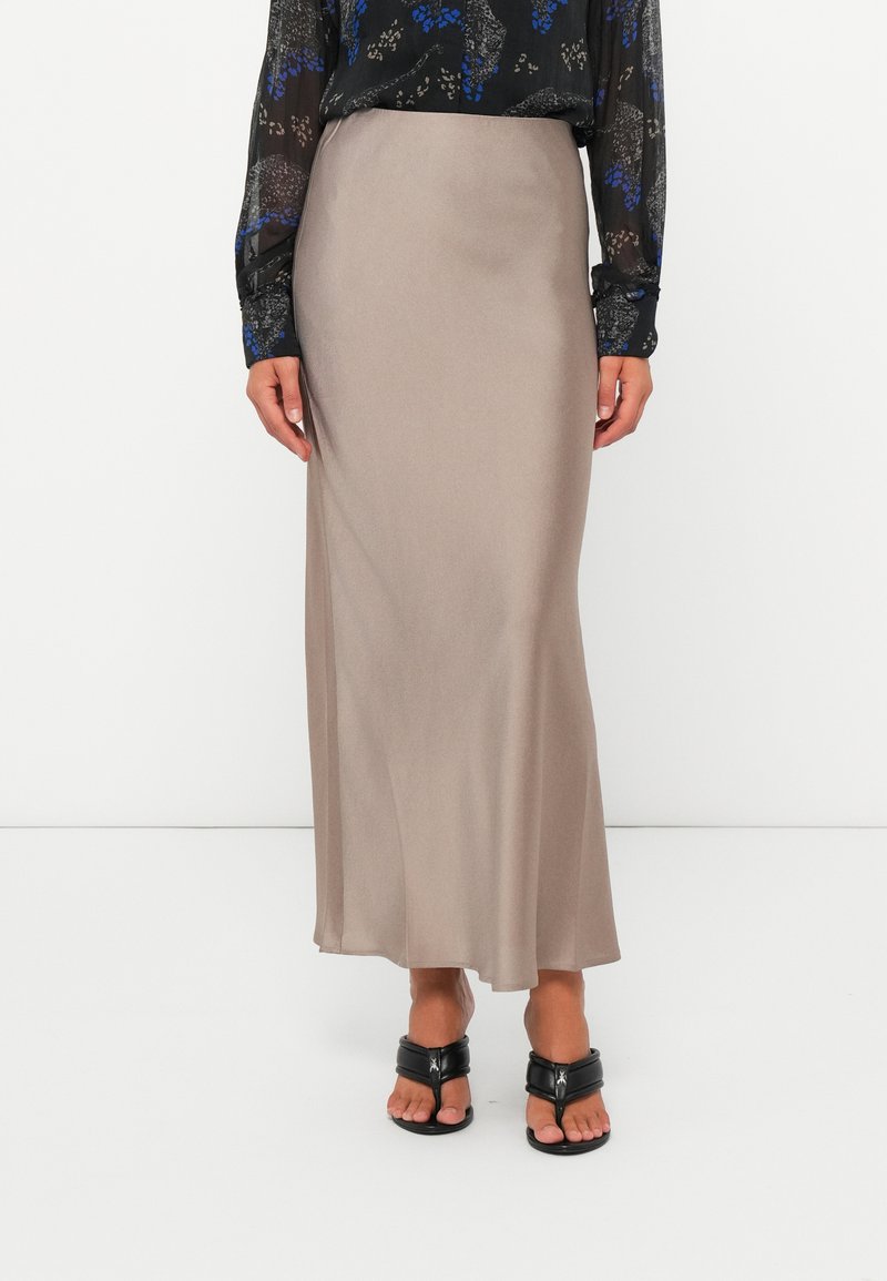 Gonna lunga in seta beige con una texture liscia e una leggera lucentezza, abbinata a una blusa nera a fantasia e sandali neri.