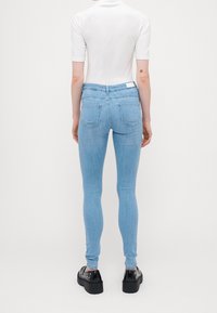 Jeans skinny de mezclilla azul claro con una cintura alta, que cuentan con bolsillos traseros y un diseño limpio. Combinados con zapatos de plataforma negros.