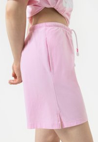 Roze katoenen shorts met een elastische tailleband en trekkoord. Voorzien van zijsplitten aan de zoom voor extra bewegingsvrijheid en comfort.